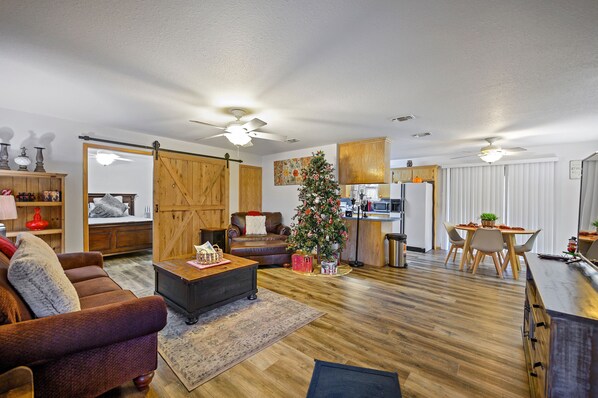 A spacious living area with a wooden floor, a dining table with chairs, a fireplace, and a Christmas tree.