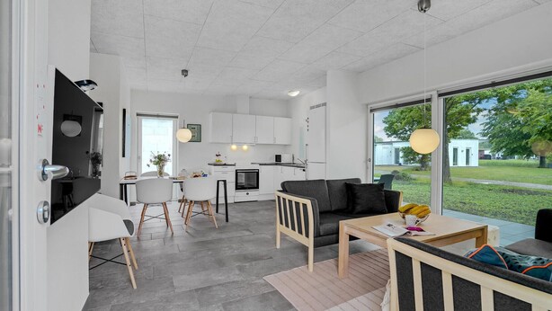 Eine moderne Küche mit weißen Schränken, ein Essbereich mit Tisch und Stühlen sowie ein großes Fenster mit Blick ins Freie.