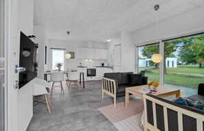 Een moderne keuken met witte kasten, een eethoek met een tafel en stoelen, en een groot raam met uitzicht op de omgeving.