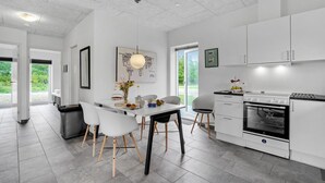Eine moderne Küche mit weißen Schränken, einem Essbereich mit Stühlen und einem großen Fenster.