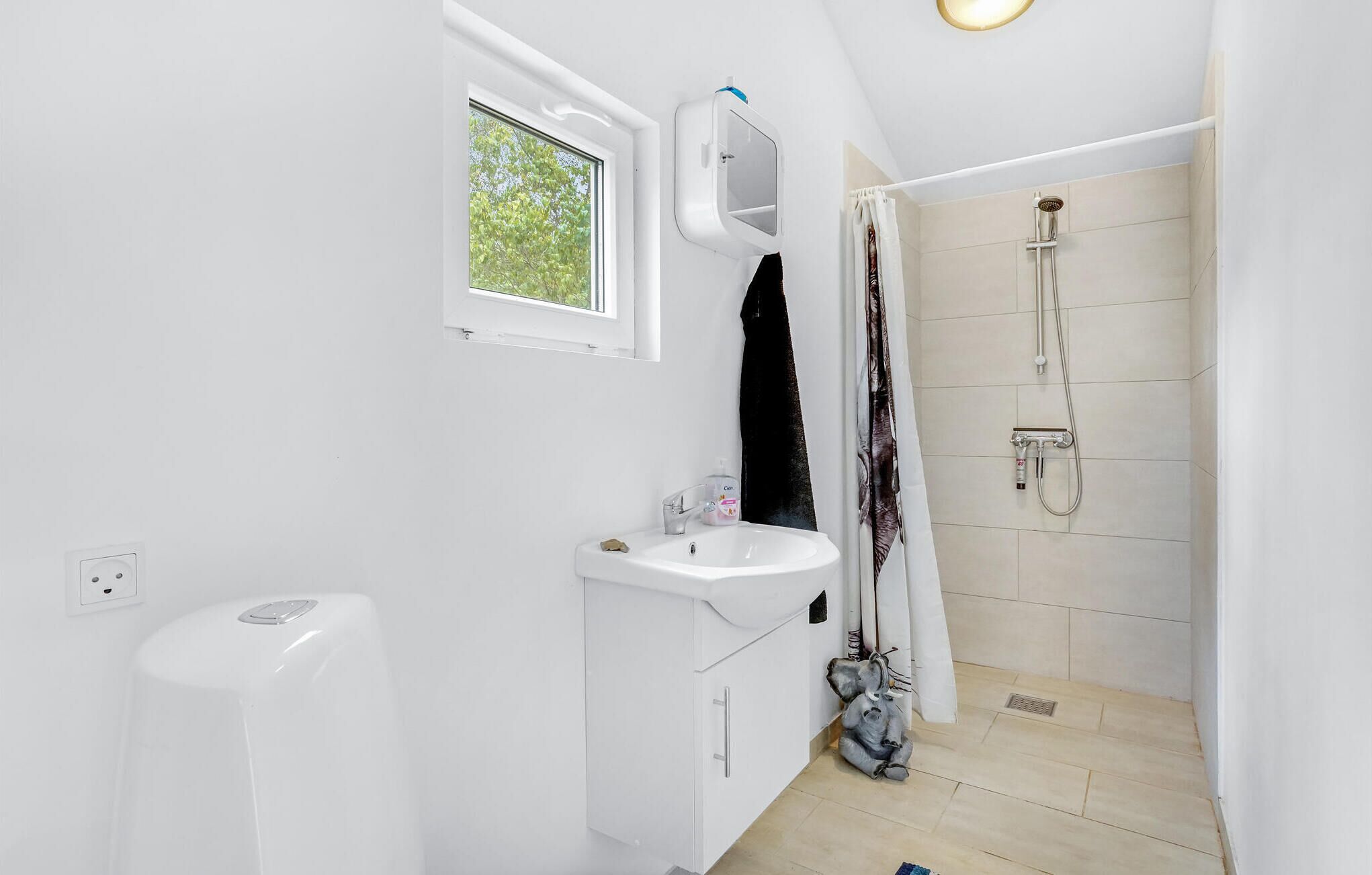 A small, white bathroom with a window, a sink, a shower, and a toilet.