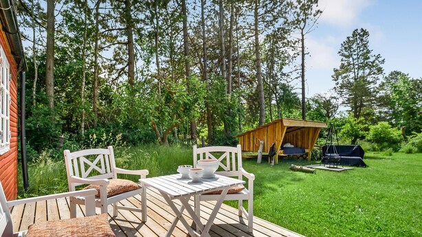 Une terrasse en bois avec une table et des chaises, une petite construction en bois et une balançoire.
