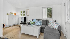 Un salon moderne avec un canapé gris, une table basse blanche et un meuble. On y trouve des fenêtres avec des rideaux, un radiateur et une porte sur laquelle est accrochée une serviette.