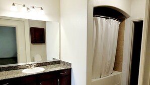 Ein Badezimmer mit Marmor-Waschtisch, dunklen Holzschränken, einem großen Spiegel und einer Dusche mit weißer Duschvorhang.