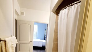 Ein schmaler Flur mit einer Badewanne, einer Tür zu einem Schlafzimmer und einem Handtuchhalter mit Handtüchern.