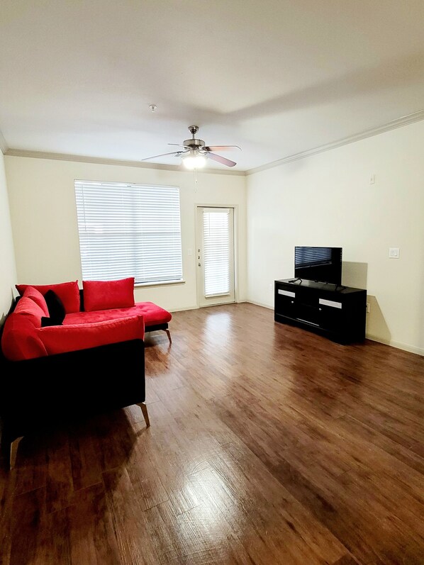 A living room with a red sofa, a ceiling fan, and a black entertainment unit. - Lovely One bedroom rental unit with pool and patio. (Houston)