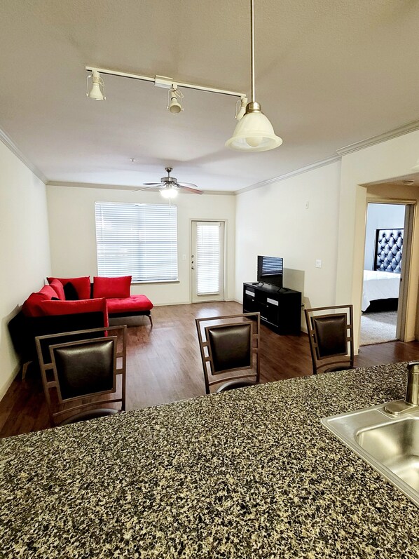 A modern kitchen with granite countertops, a dining area with a red sofa, and a ceiling fan.