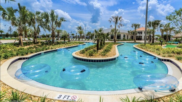 A pool with multiple water slides and inflatable rings, surrounded by palm trees and a clear sky.