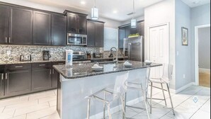 A modern kitchen with dark cabinets, a granite countertop, stainless steel appliances, and a central island with bar stools.