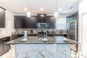 A modern kitchen with dark cabinets, granite countertops, stainless steel appliances, and a central island with bar stools.