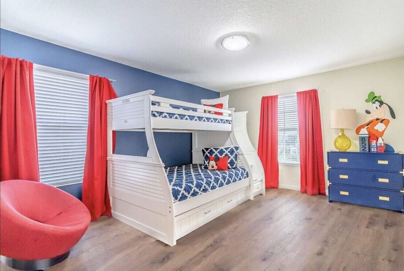 A bunk bed with a patterned mattress, a red chair, and a blue dresser with drawers.