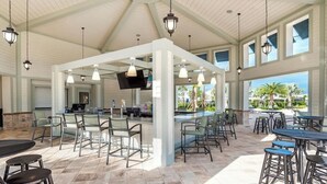 A spacious outdoor bar area with multiple seating options, including bar stools and chairs, under a high ceiling with hanging lights.