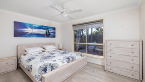 A bedroom with a bed, a nightstand, a dresser, a ceiling fan, and a window with a view of the outdoors.