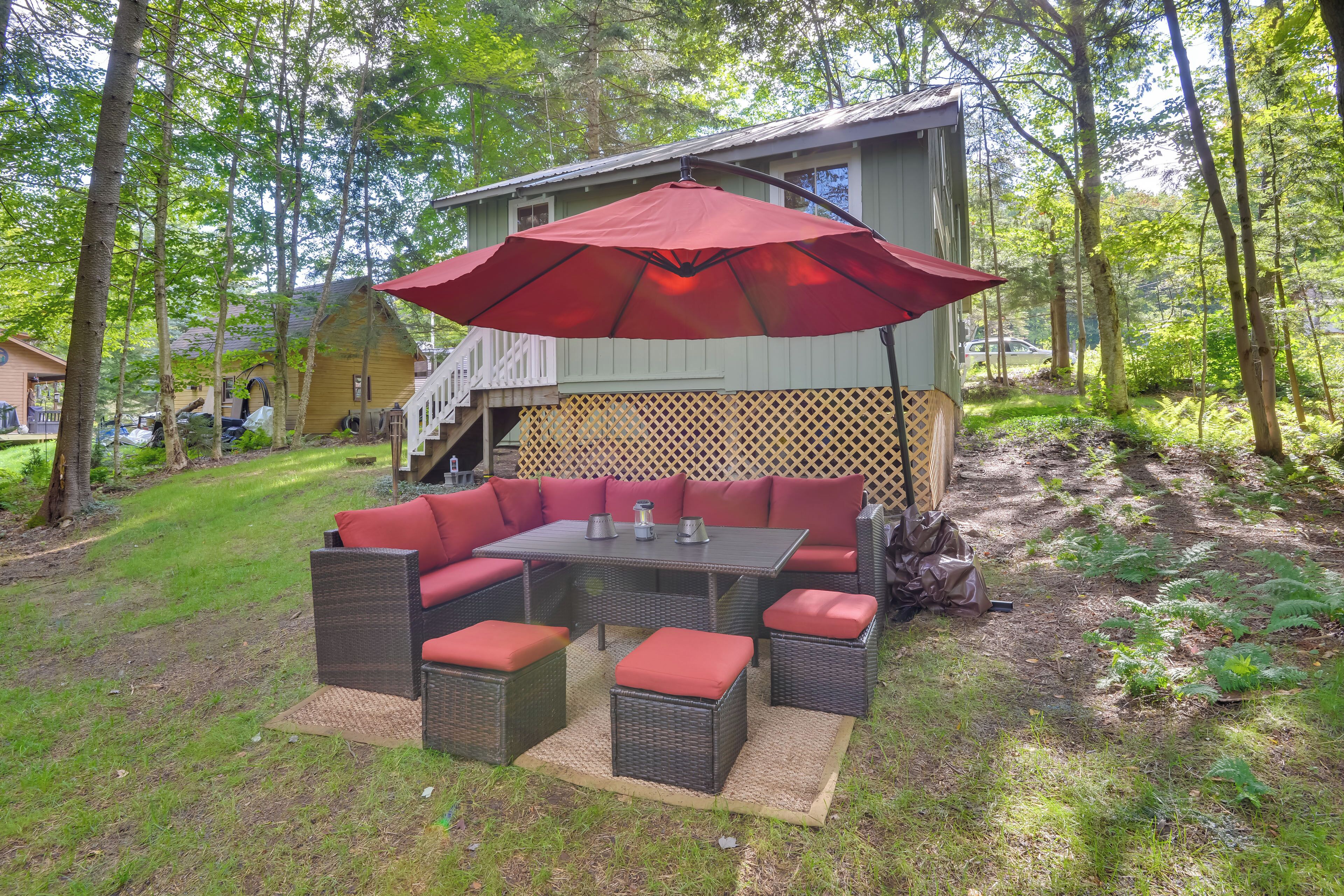 Ett takförsett utomhusområde med bord och stolar, ett rött parasoll och ett trädäck.