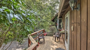 Eine Holzterrasse mit zwei Stühlen und einem kleinen Tisch, umgeben von Pflanzen und einem Haus.