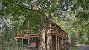 Eine rustikale Holzhütte mit einer Holzterrasse, umgeben von üppiger Vegetation und Bäumen.