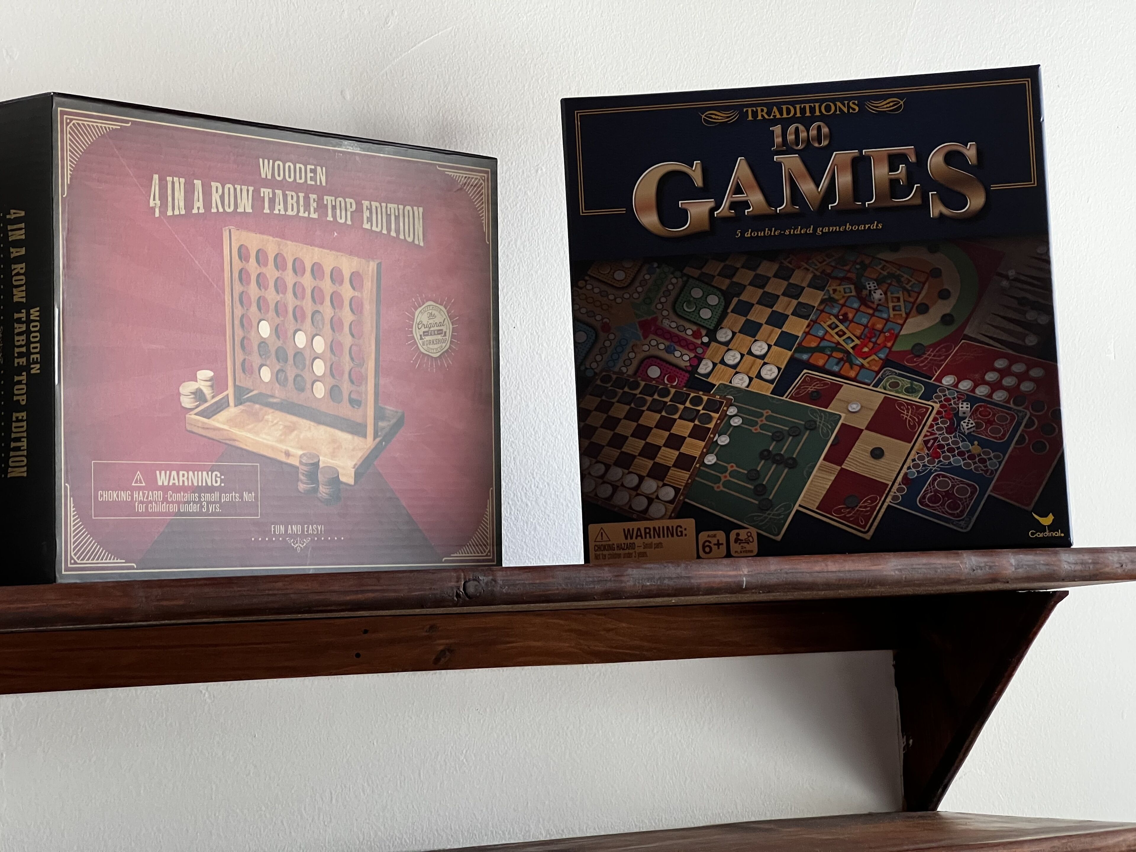 Two board games, 'Wooden 4 in a Row Table Top Edition' and 'Traditions 100 Games', on a shelf.