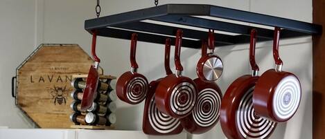 A kitchen with hanging pots and pans, a wooden box labeled 'LAVAN', and a white refrigerator.