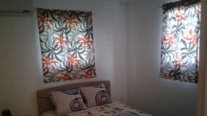 Ein Schlafzimmer mit einem Bett, einem Nachttisch und zwei Fenstern mit gemusterten Vorhängen.