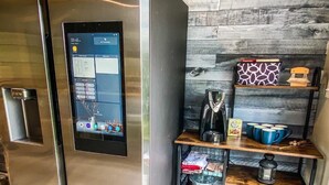 A modern kitchen with a built-in digital interface on the refrigerator, wooden shelves with kitchenware, and a coffee maker. - Cozy Adirondack Loft Near Lake Champlain & George, Hiking and Historical Sites (Ticonderoga)