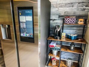 A modern kitchen with a built-in digital interface on the refrigerator, wooden shelves with kitchenware, and a coffee maker.
