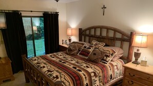 A wooden bed with a patterned bedspread, two bedside lamps, a wooden nightstand, and a cross on the wall. - Winterplace Condo Steps away from slopes (Ludlow)
