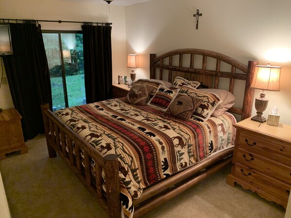 A wooden bed with a patterned bedspread, two bedside lamps, a wooden nightstand, and a cross on the wall.