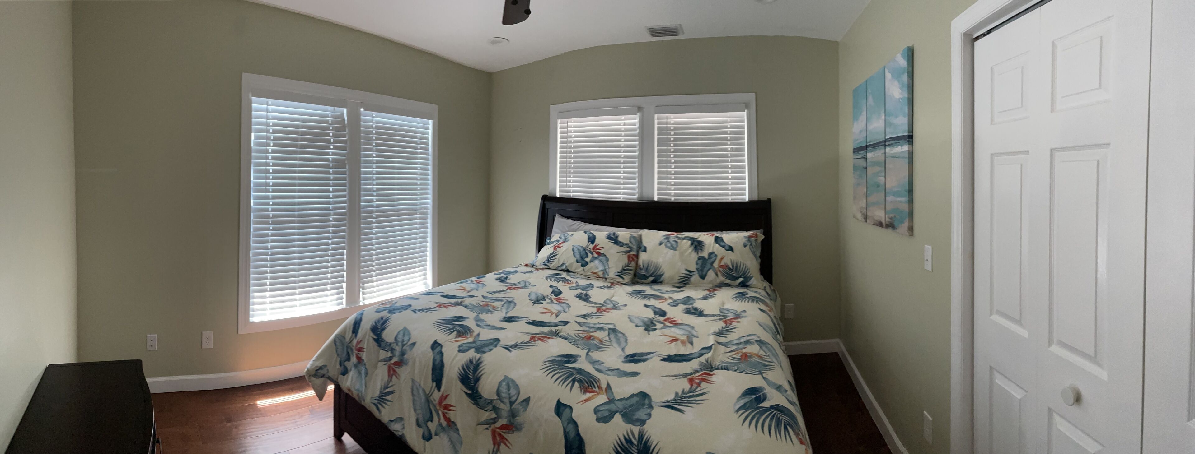 A bedroom with a bed, two windows with blinds, a door, and a painting on the wall.