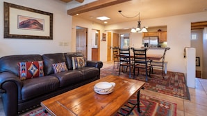 A living room with a leather sofa, a wooden coffee table, and a dining area with a chandelier. - El Corazon by Kokopelli Property Management (Santa Fe)
