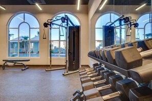 Ein Fitnessstudio mit Krafttrainingsgeräten, großen Fenstern und einer Bank.
