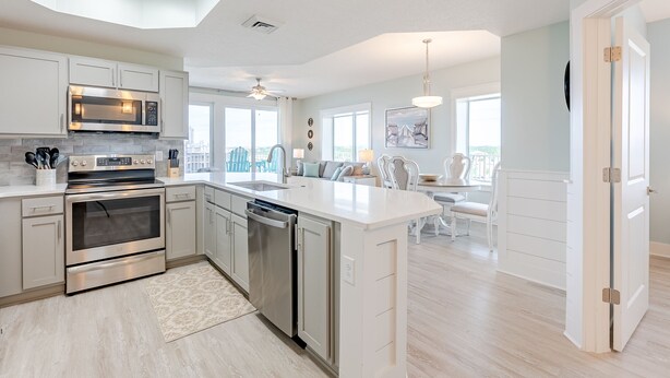 A modern kitchen with stainless steel appliances, a large island, and a dining area with a view. - End-Unit 3Bed/3Bath Condo w/ Gulf Views, Wraparound Balcony & Tiki Bar! (Panama City Beach)