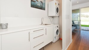 A modern kitchen with white cabinetry, a built-in washing machine, a sink, and a bucket.
