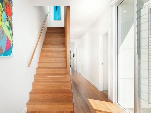 Un escalier en bois menant à un palier sur lequel est accrochée une peinture abstraite bleue.