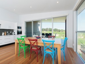 A modern kitchen with white cabinets, a wooden dining table, and colorful chairs. - 41A Ocean Avenue - reserve front Ocean Views (Anna Bay)