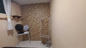 A small bathroom with a tiled wall, a fan, a shelf with a decorative item, and a hanging shower curtain.