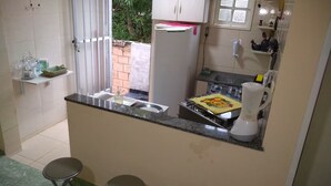 A compact kitchen with a refrigerator, a sink, and a stove. There are two stools and a window with a view of the outside.