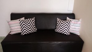 A black sofa with two patterned pillows against a plain wall.