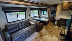 A compact RV interior with a sofa, a small dining table, and a kitchenette area. - Biloxi Bay Adventure: Stay in Our Comfortable Camper Rental (Biloxi)