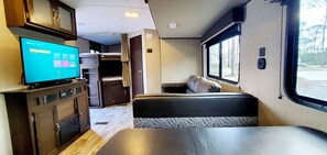 Interior compacto de una autocaravana con kitchenette, televisor, zona de estar y ventana con vistas al exterior.