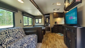 A compact RV interior with a sofa, kitchenette, and a TV displaying a home screen. - Biloxi Bay Adventure: Stay in Our Comfortable Camper Rental (Biloxi)