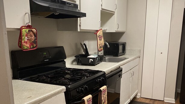 A kitchen with white cabinets, a stove, a microwave, and a wooden floor. - Braves Stadium  (Smyrna)