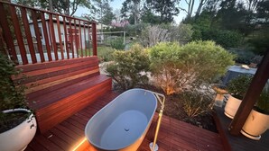 A wooden deck with a built-in bathtub, surrounded by greenery and a metal fence. - HAILEY@KURRAJONG - stylish and delightful. SPECIALS ON NOW ! (Kurrajong)