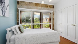 A bedroom with a bed, white walls, a stone wall, and a window with blinds. - HAILEY@KURRAJONG - stylish and delightful. SPECIALS ON NOW ! (Kurrajong)