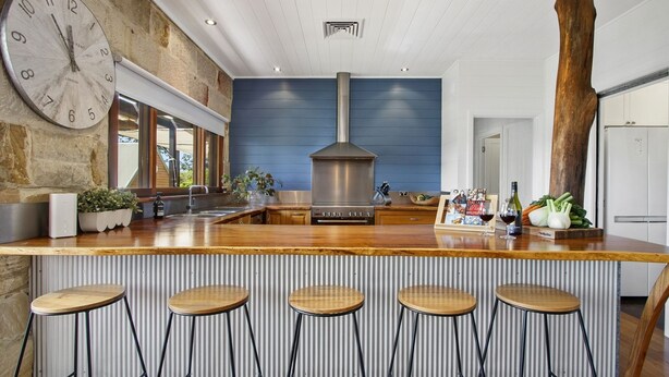 A modern kitchen with a central island, bar stools, a large clock, and a rustic wooden beam. - HAILEY@KURRAJONG - stylish and delightful. SPECIALS ON NOW ! (Kurrajong)