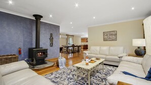 A living room with a fireplace, a sofa, a coffee table, and a dining area in the background. - HILLDO - Beautiful home set amongst the tree  - SPECIALS ON NOW ! (Kurrajong Heights)