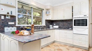 A kitchen with white cabinets, a marble countertop, a window with a view of trees, a stove, and a sink.
