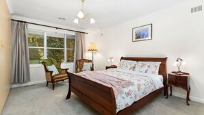 A bedroom with a large bed, a chair, a bedside table, a lamp, and a window with curtains.