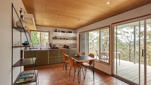 Uma cozinha moderna com armários de madeira, uma mesa de jantar com cadeiras e uma grande porta de vidro deslizante que dá para um deck externo.