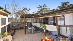 Un patio rústico al aire libre con un brasero, asientos y un autobús antiguo convertido en espacio habitable.