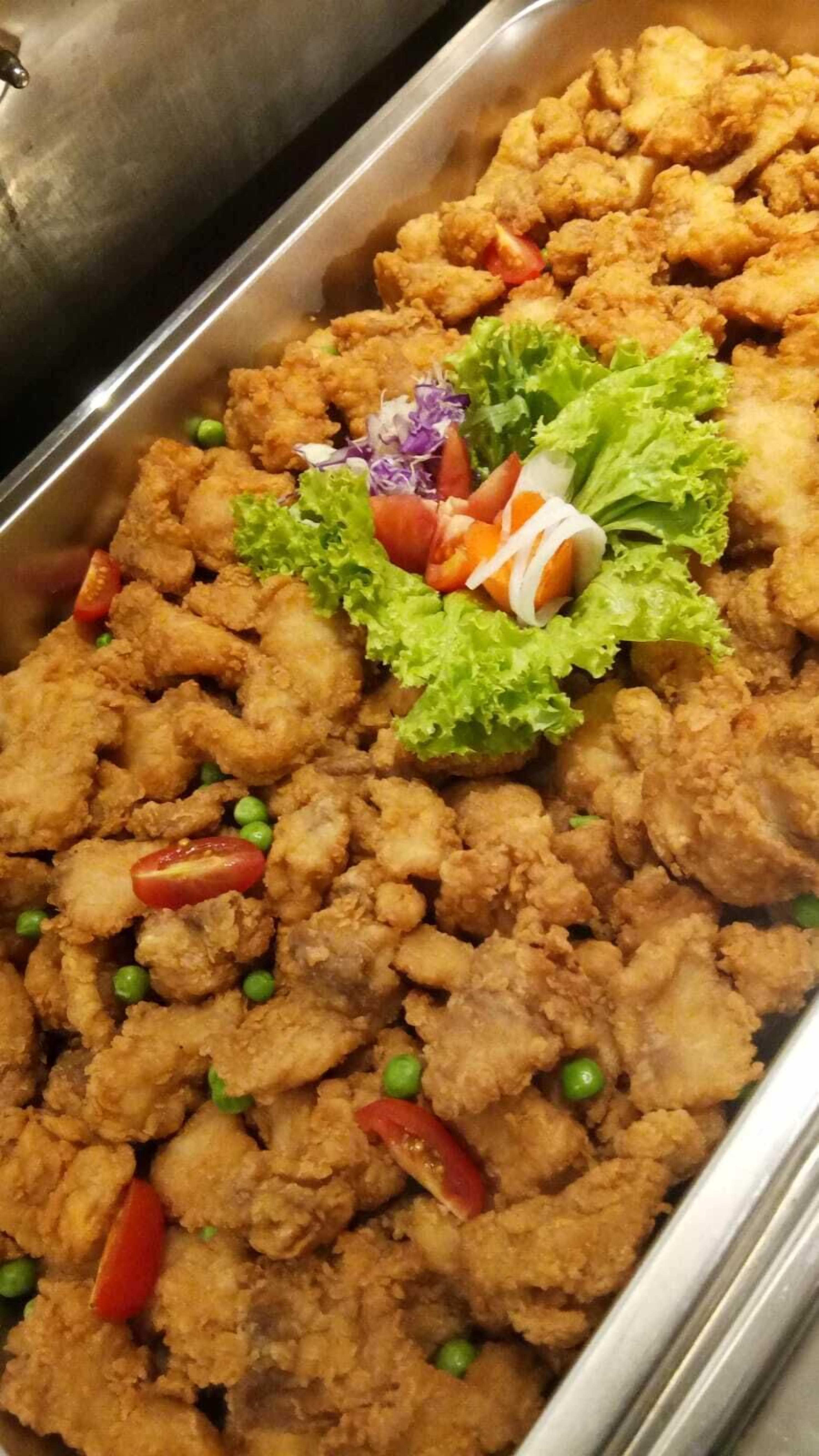 Una bandeja de buffet con trozos de pollo frito, lechuga, tomates y guisantes.